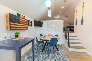 A dining area with a round table, chairs, and a small plant. There is a staircase with a railing and a wall-mounted TV. - Walk to Water with Hot Tub! (Yarmouth)