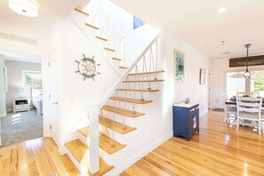 A modern interior with a wooden staircase, a ship's wheel decoration, and a dining area with a chandelier. - Walk to Water with Hot Tub! (Yarmouth)