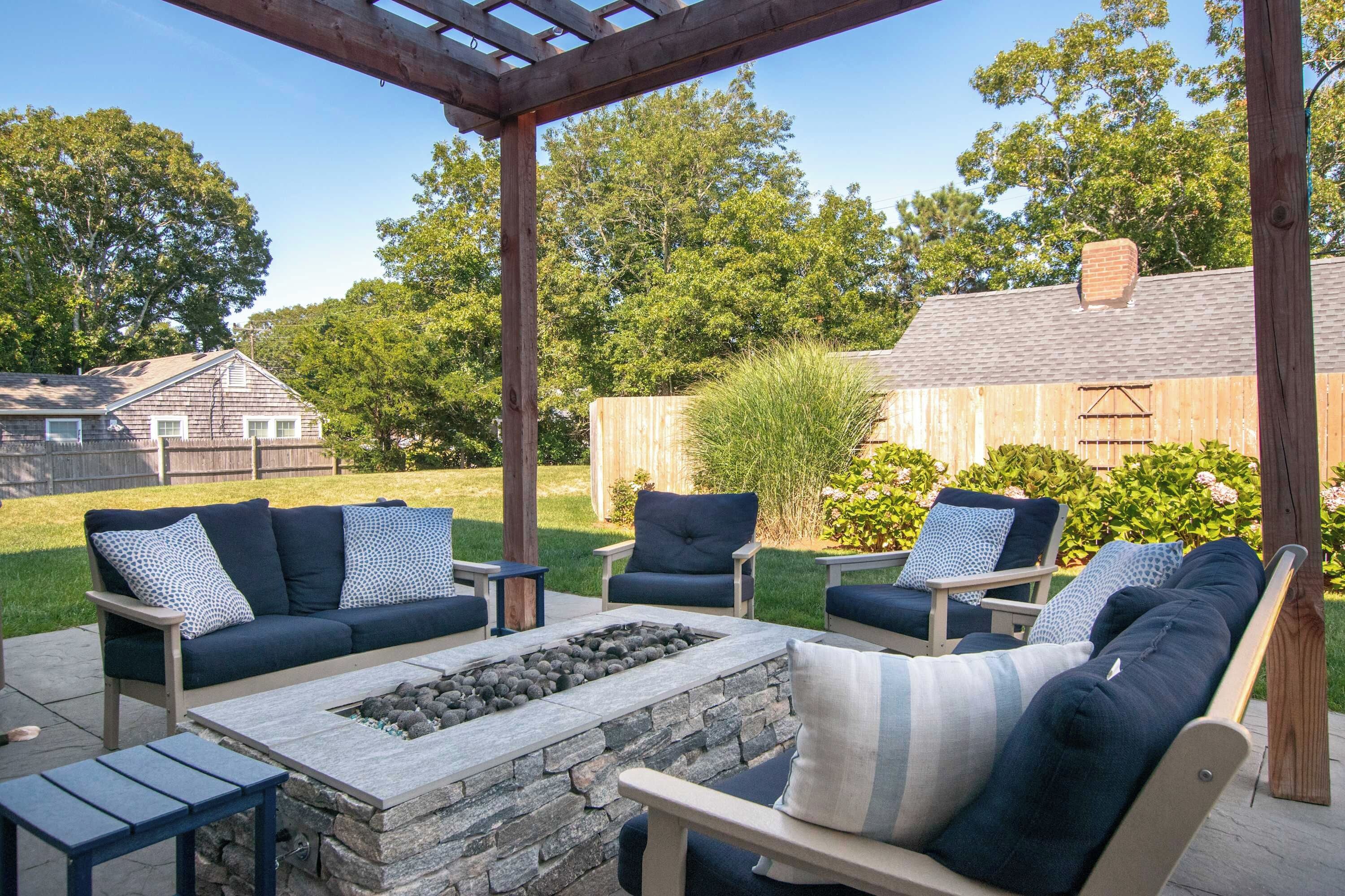 An outdoor patio with a stone fire pit, two sofas, and two chairs.