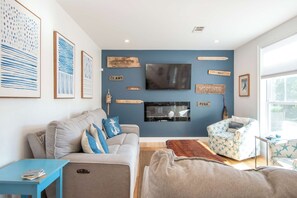 A living room with a blue accent wall, a flat-screen TV, and nautical-themed decor. - Walk to Water with Hot Tub! (Yarmouth)
