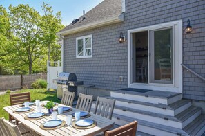 Une façade de maison avec un patio couvert, un barbecue et une table à manger pour quatre personnes.