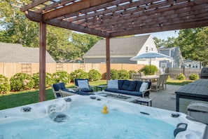 A backyard with a hot tub, outdoor furniture, and a pergola.