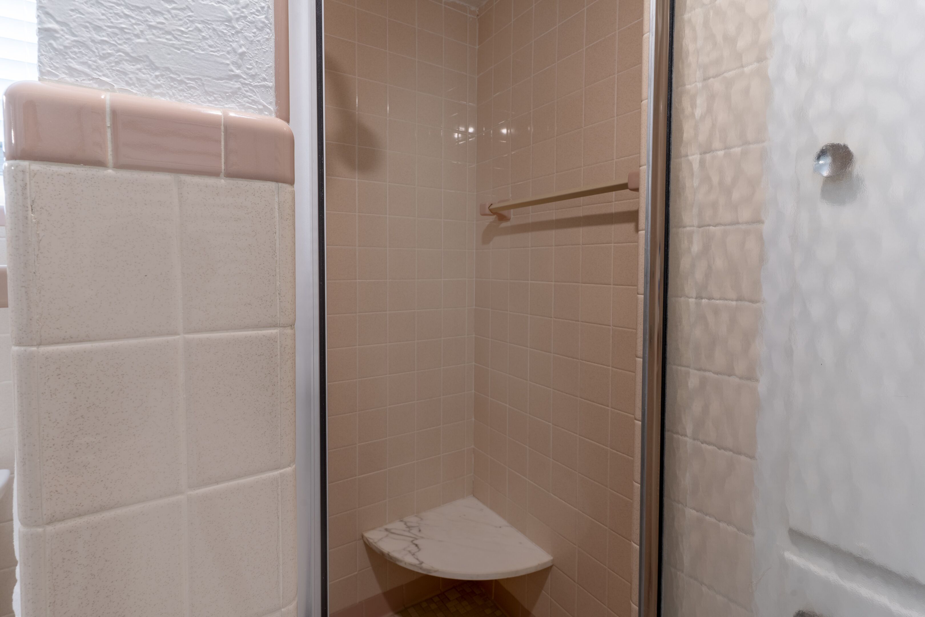 Une salle de bain avec une douche à parois de verre, des toilettes blanches et des murs recouverts de carreaux beiges.