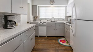 Una cocina compacta con armarios blancos, estufa, cafetera y un reloj en la pared.