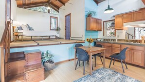 Ampla sala de estar com sofá, mesa de jantar, cadeiras, armários de madeira e cozinha com bancada e pia.