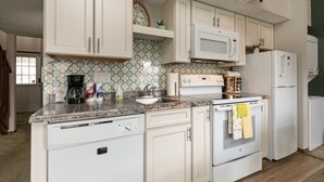 Una cocina con armarios blancos, microondas, estufa y refrigerador.