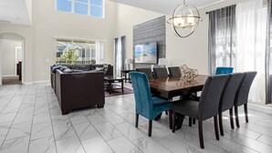 Een ruime woonkamer met een donkerbruine bank, een eettafel met stoelen en een groot raam met gordijnen.