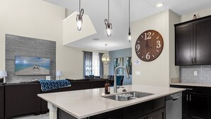 Een moderne keuken met een groot kookeiland, donkere kasten en een grote wandklok.