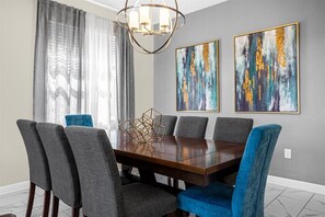 Une salle à manger avec une table rectangulaire, six chaises grises à revêtement rembourré et deux tableaux abstraits accrochés au mur.