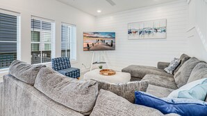 A modern living room with a gray sectional sofa, a small round coffee table, and a flat-screen TV mounted on the wall.