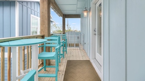 A covered porch with turquoise chairs and a wooden table, a door with a window, and a light fixture above the door.