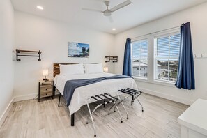 Ein Schlafzimmer mit Bett, Nachttischen, Deckenventilator, einem Fenster mit Vorhängen und Blick auf Gebäude.