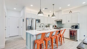 A modern kitchen with white cabinets, stainless steel appliances, and a central island with orange bar stools.