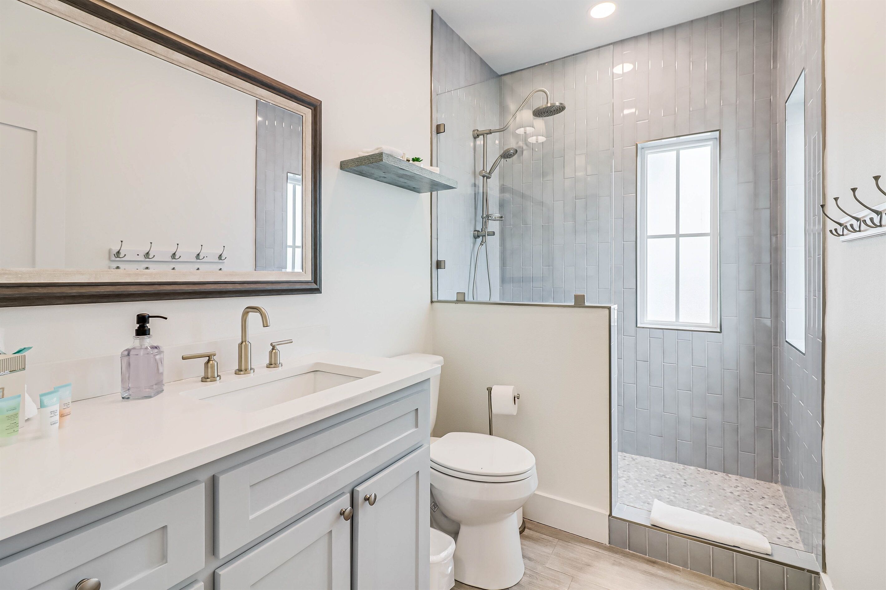 Un baño moderno con tocador blanco, un espejo grande, ducha con cerramiento de vidrio y un inodoro.