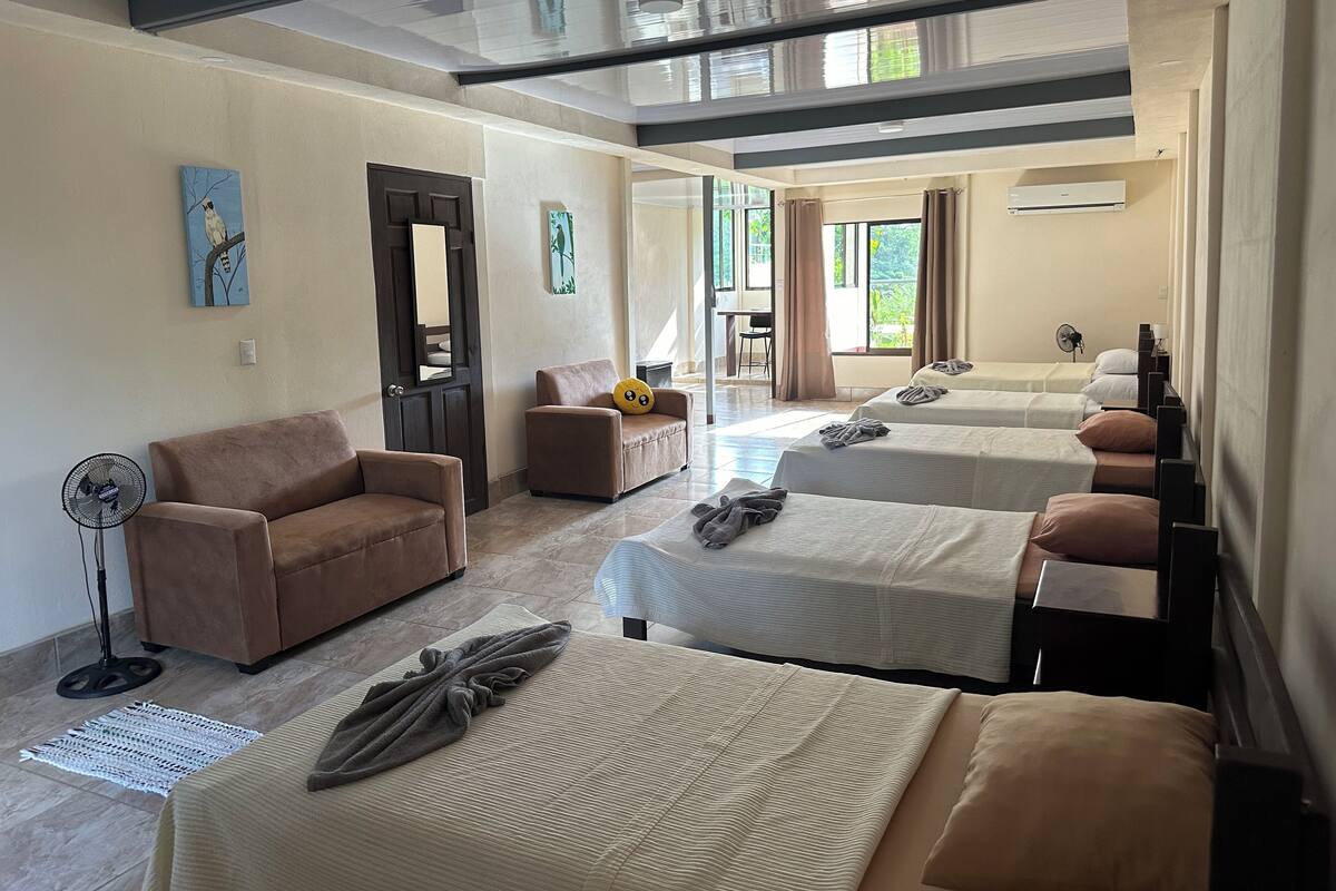 Ein Hotelzimmer mit einer Couch, zwei Betten, einem Ventilator und Bildern an den Wänden.