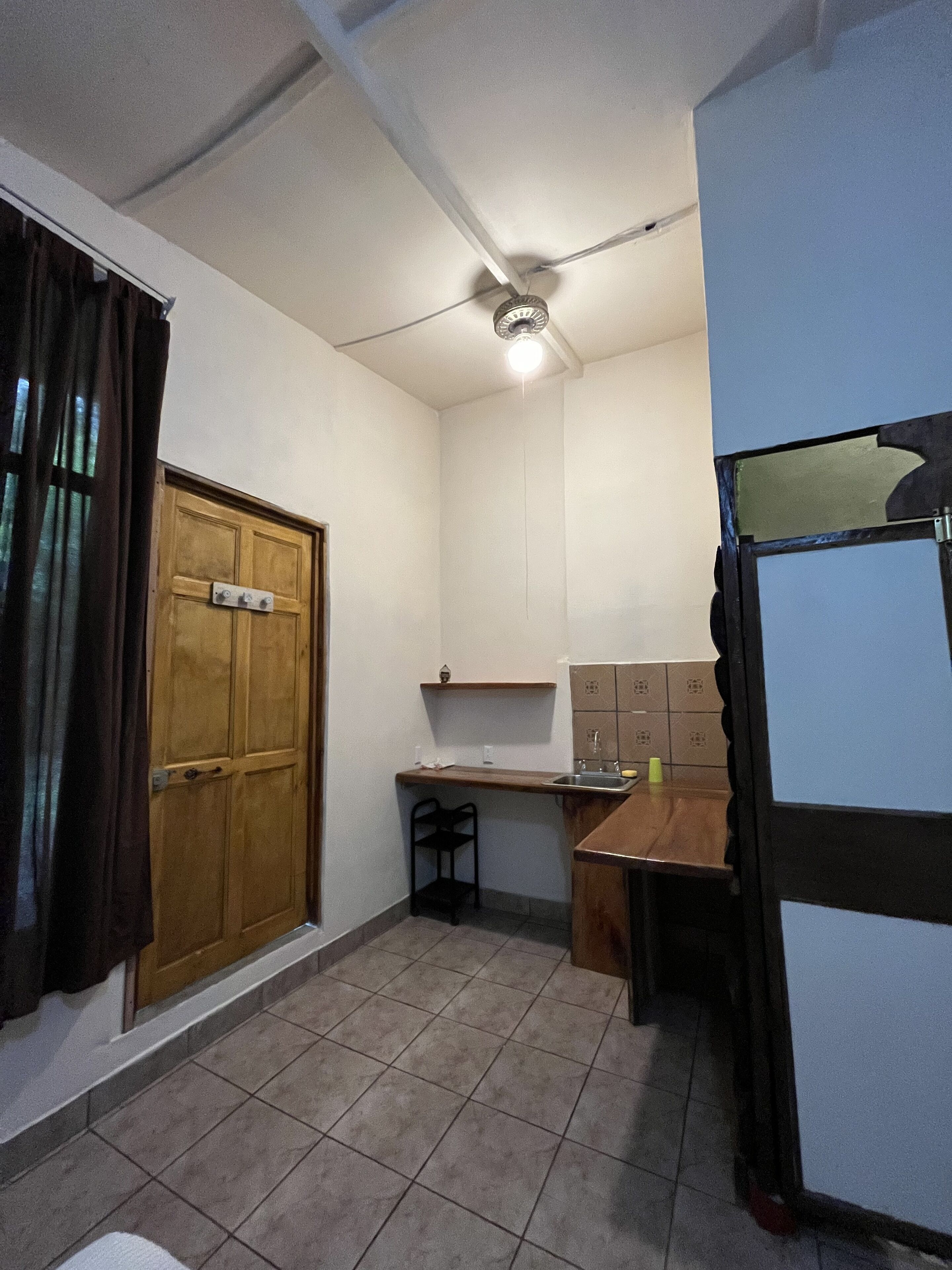 A small, compact kitchen with a wooden door, a small table, and a ceiling fan.