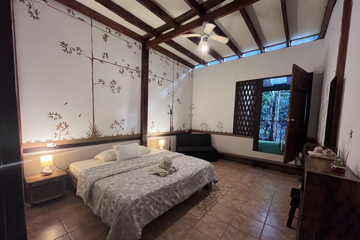 Ein Schlafzimmer mit Bett, Nachttischlampen, Deckenventilator und einem Fenster mit Blick ins Freie.