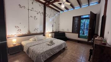 Une chambre à coucher avec un lit, des lampes de chevet, un ventilateur de plafond et une fenêtre donnant sur l’extérieur.