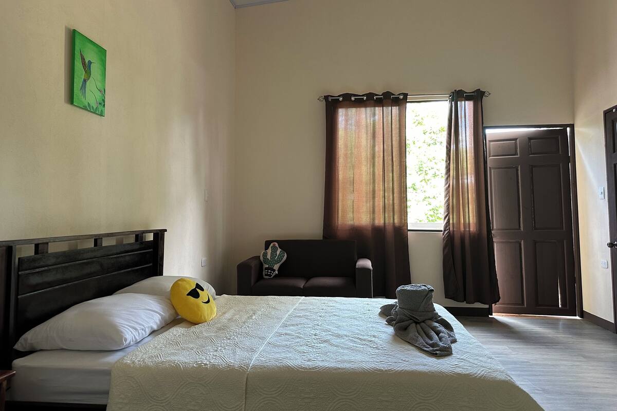 Ein Hotelzimmer mit Bett, Stuhl, Vorhängen am Fenster und einer Tür.
