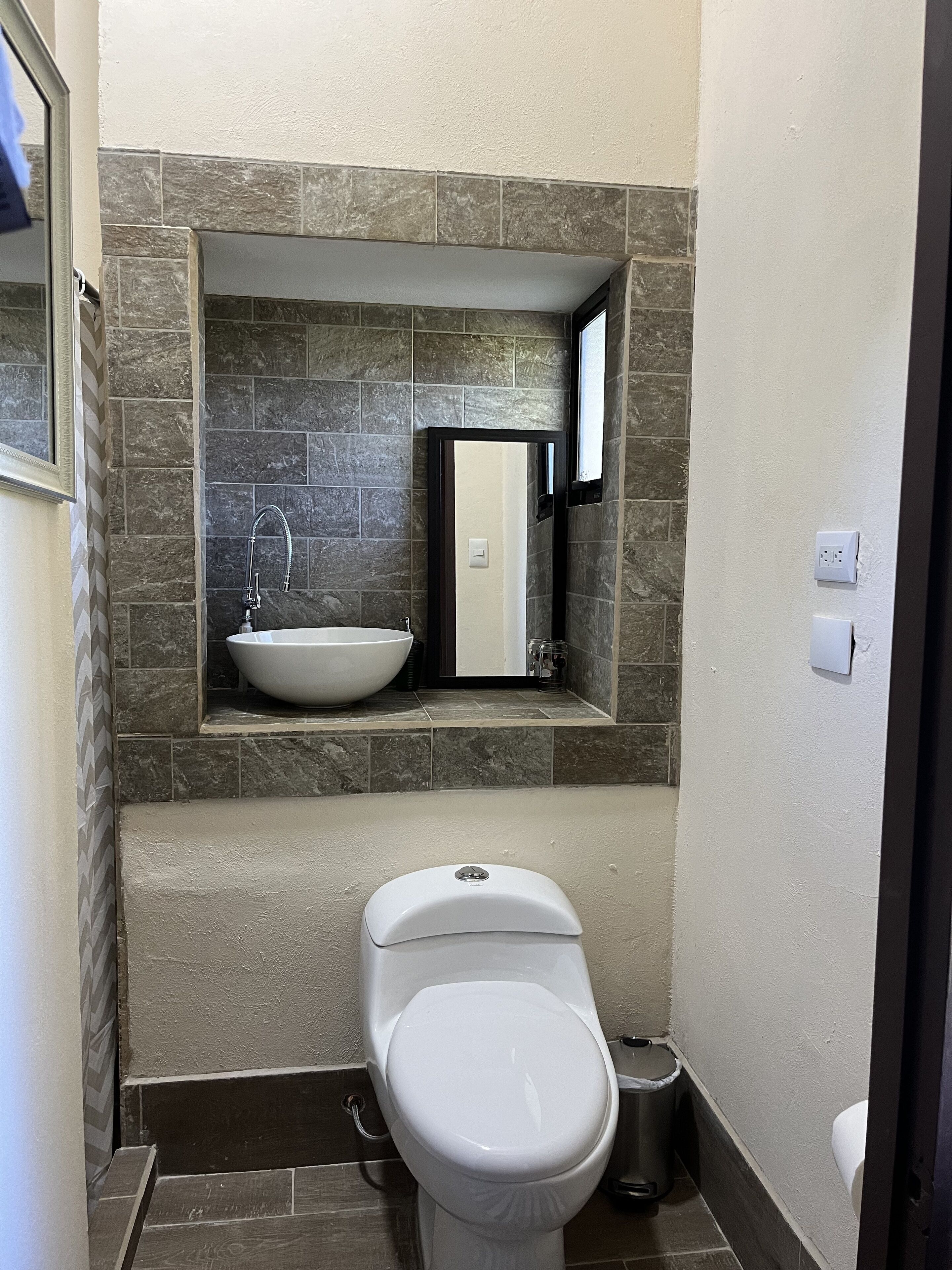 A compact bathroom with a white toilet, a vessel sink, and a mirror above the sink.