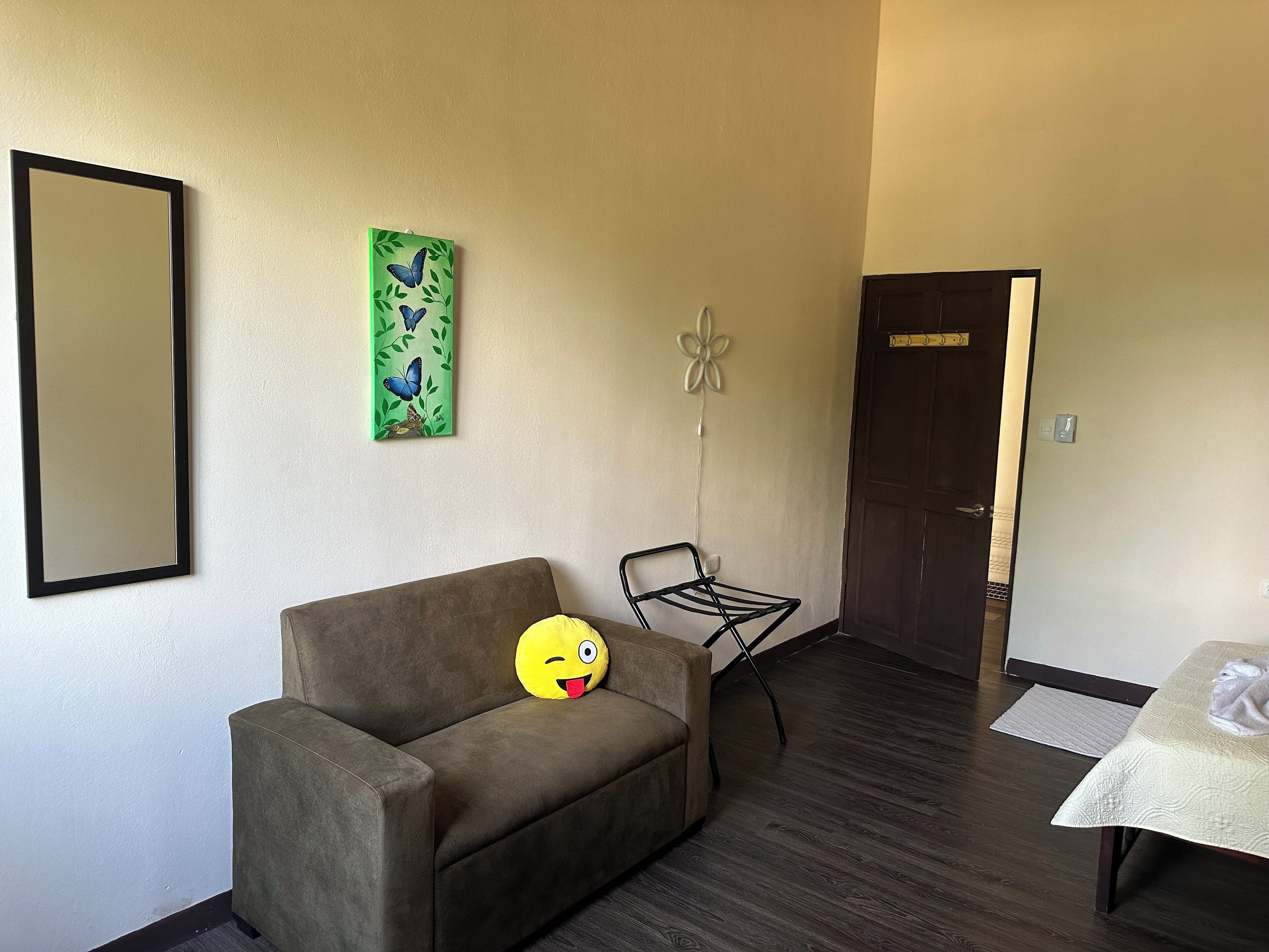 Une pièce comprenant un canapé, une petite table, un miroir, un tableau vert et une porte.