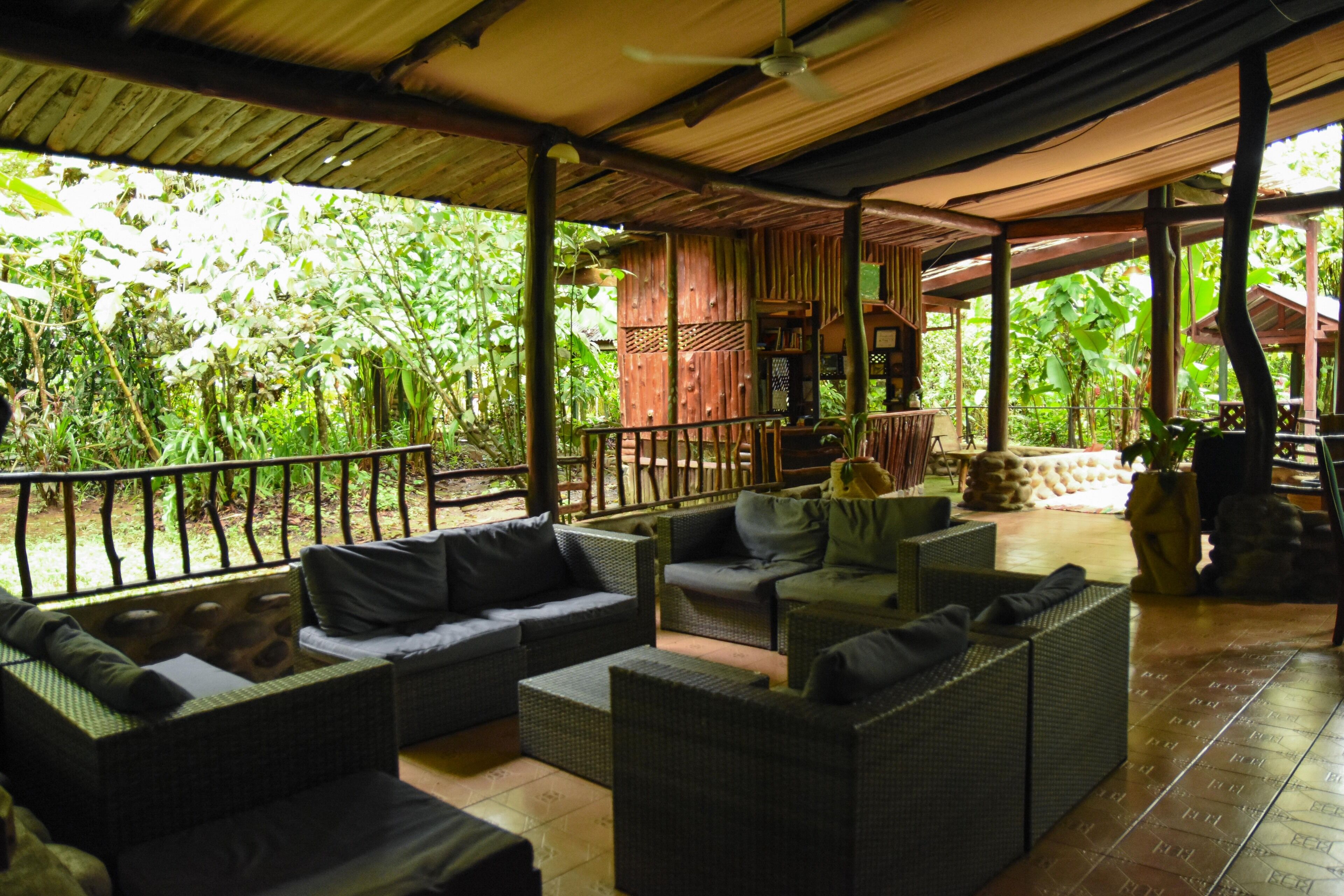 A covered outdoor seating area with wicker furniture and a view of lush greenery.