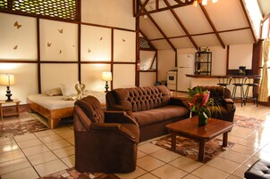 Uma sala ampla com uma cama, sofás, uma mesa de centro e uma cozinha ao fundo.