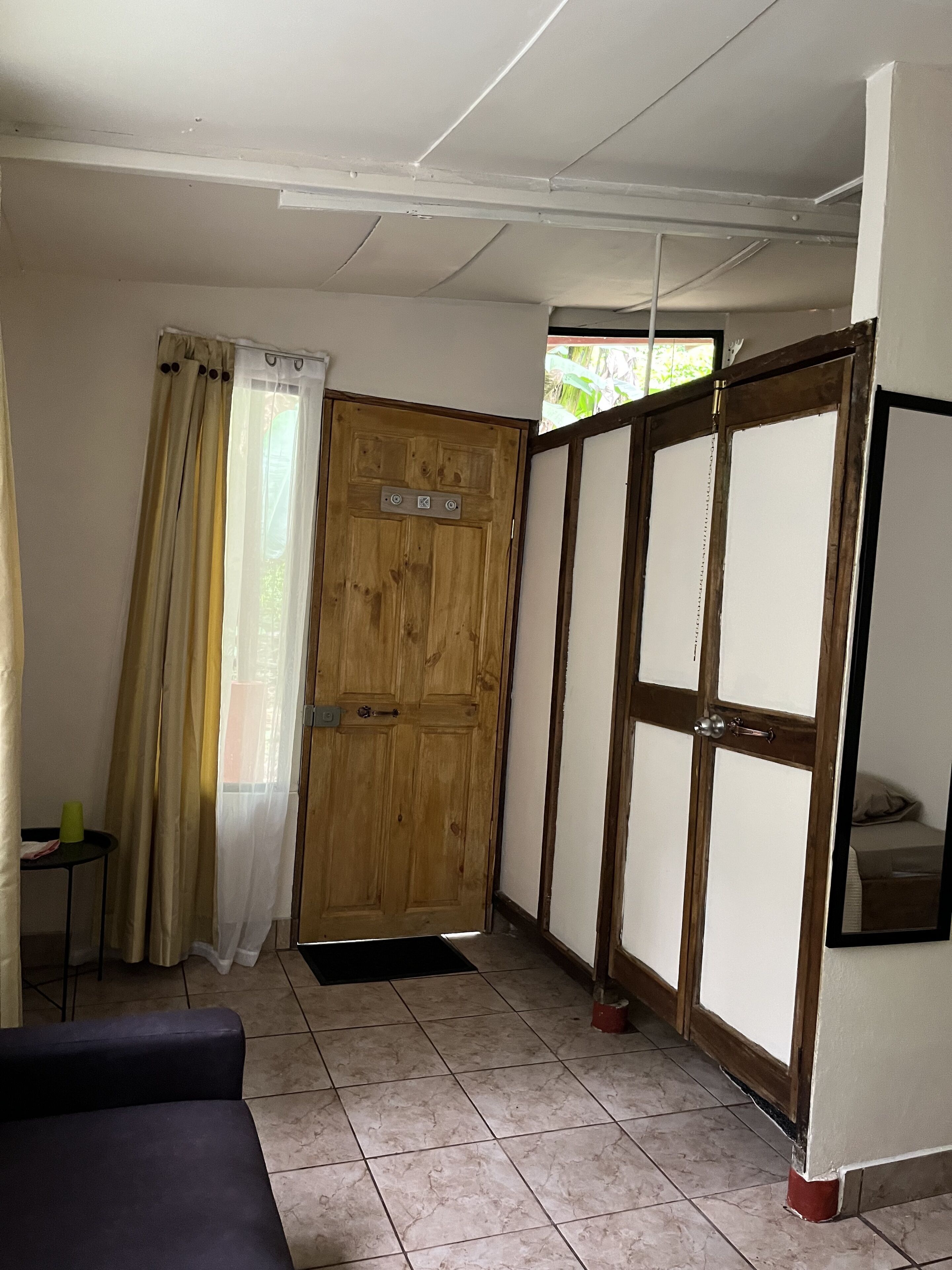 A room with a wooden door, a black sofa, and a tiled floor.