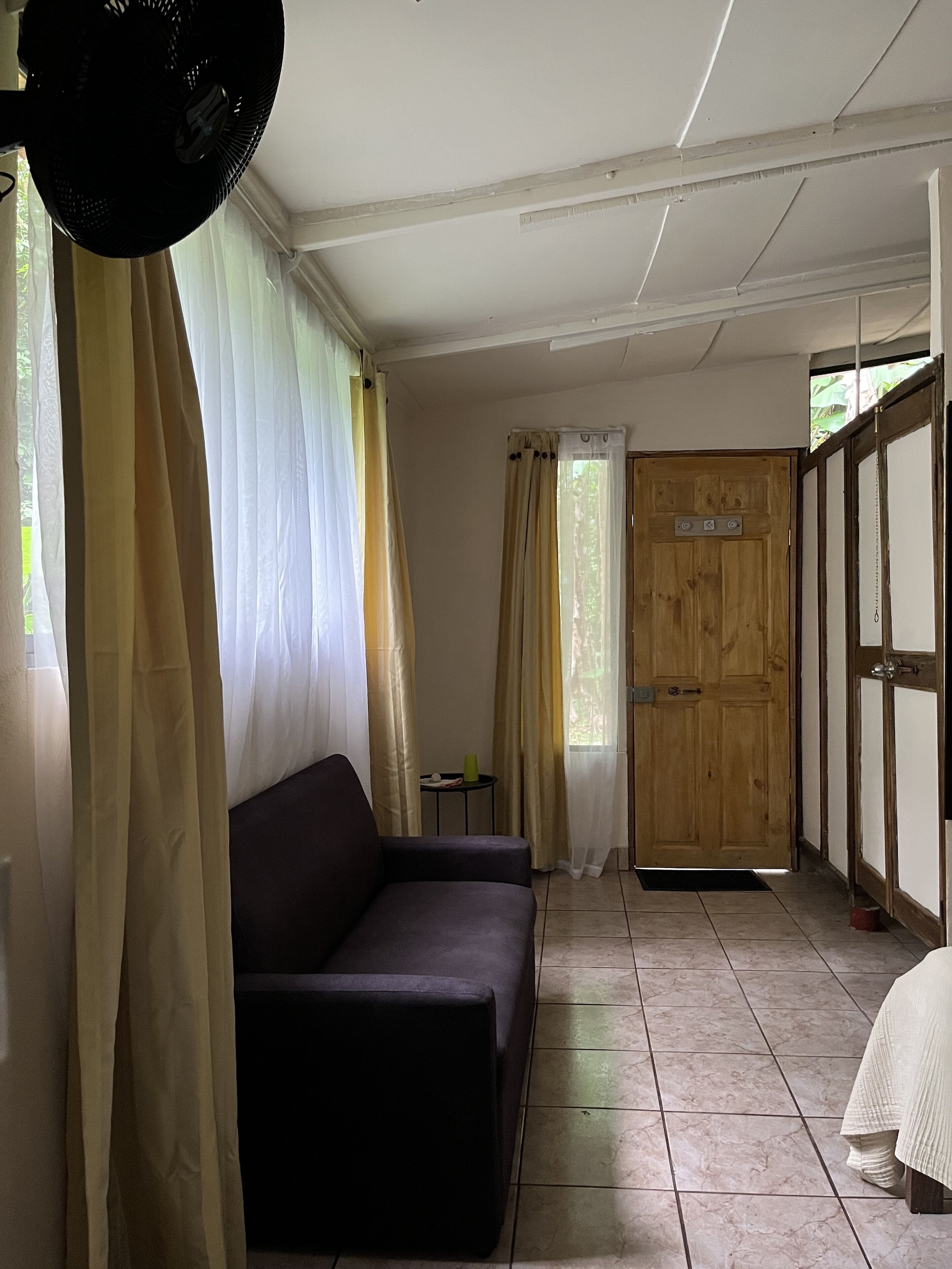 A room with a dark-colored sofa, a wooden door, and a tiled floor.