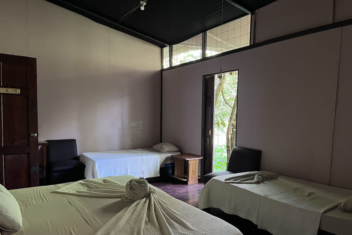 Ein Zimmer mit zwei Betten, einem Holzstuhl, einem kleinen Tisch und einer Tür.