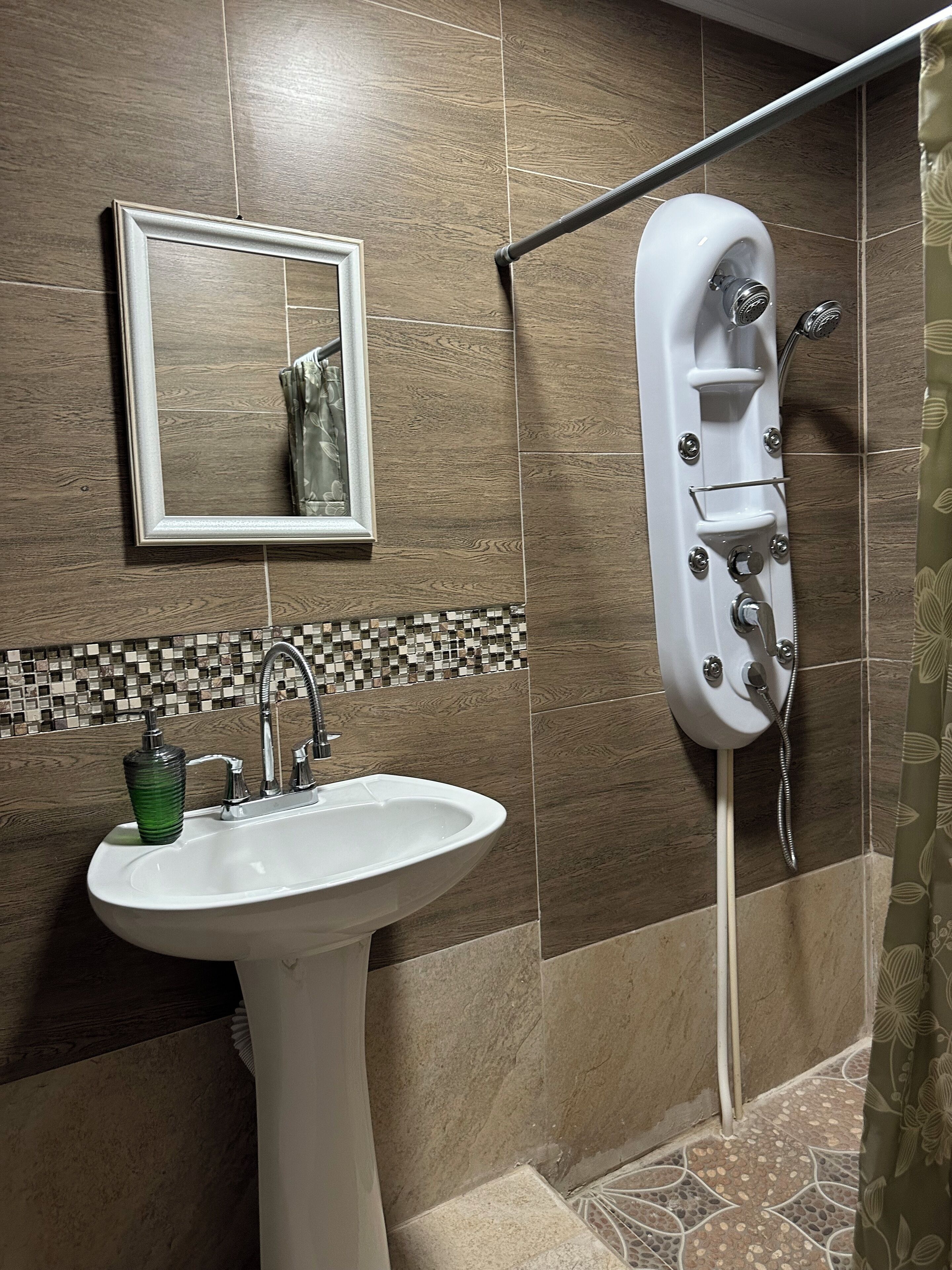Un bany amb un lavabo, mirall, dutxa i parets revestides de rajoles.