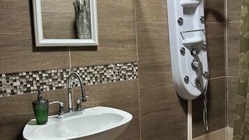 Un bany amb un lavabo, mirall, dutxa i parets revestides de rajoles.
