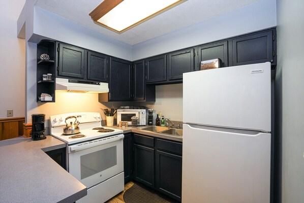 A compact kitchen with dark cabinets, a white refrigerator, a stove, a microwave, and a coffee maker.