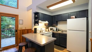 Une cuisine moderne avec des meubles de couleur sombre, un réfrigérateur blanc, une cuisinière et un grand îlot central doté de tabourets.