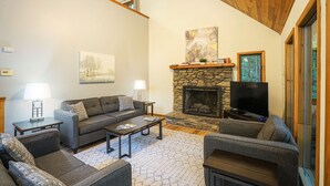 Un salon chaleureux avec une cheminée en pierre, un téléviseur à écran plat et des fauteuils confortables.