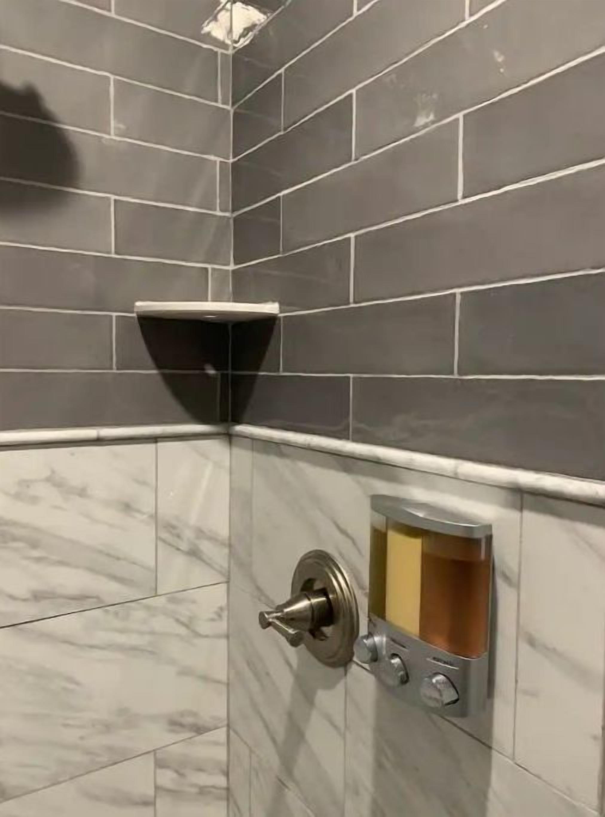 A corner of a bathroom with dark gray tiles and a marble floor.