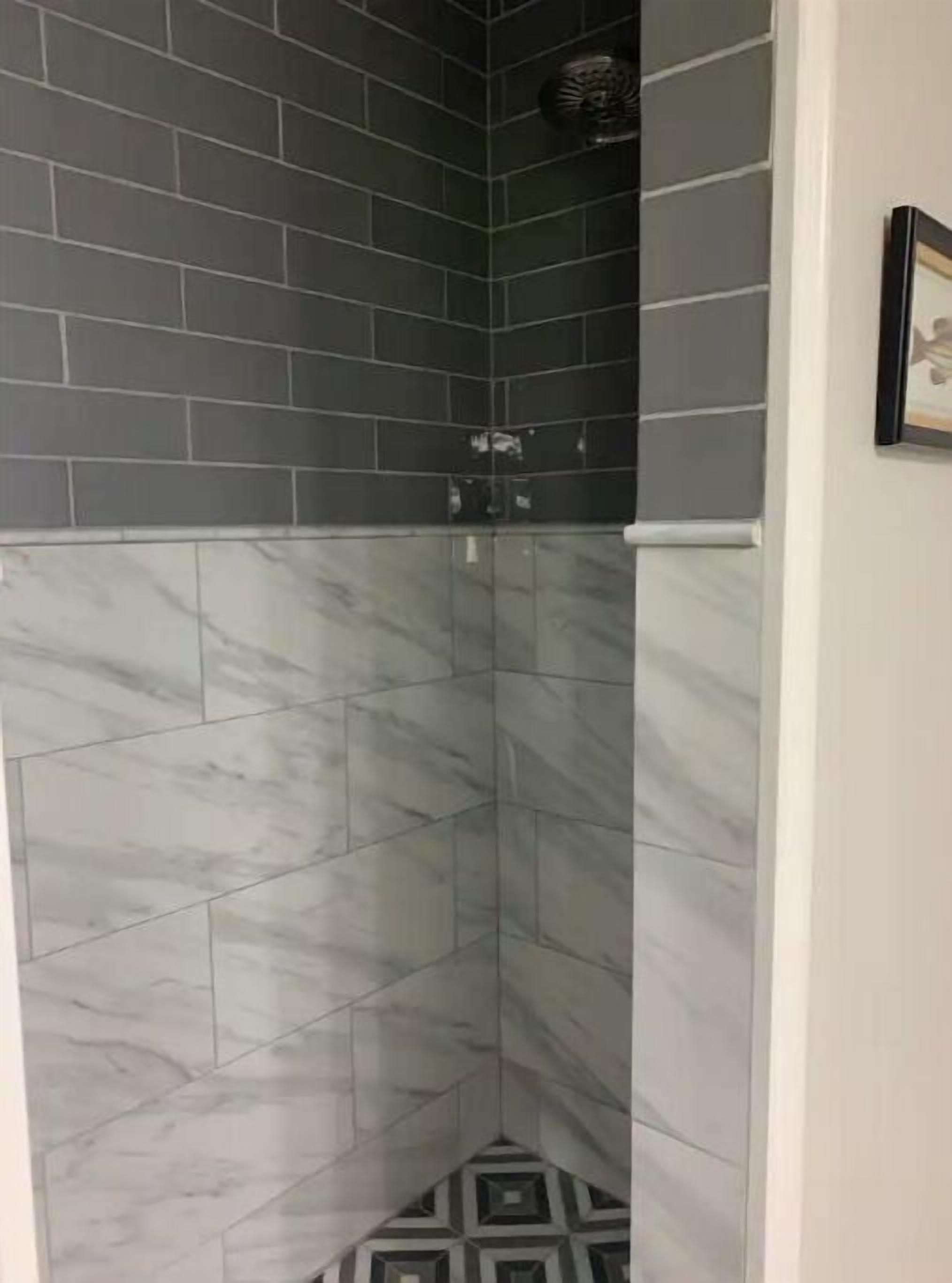 A corner shower with dark grey tiles and white marble patterns.