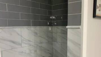 A corner shower with dark grey tiles and white marble patterns.
