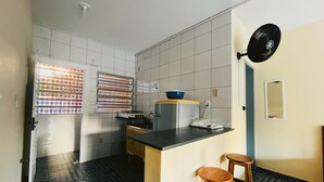 Een compacte keuken met een gasfornuis, een blauwe kom op het aanrecht en een zwarte ventilator aan de muur.