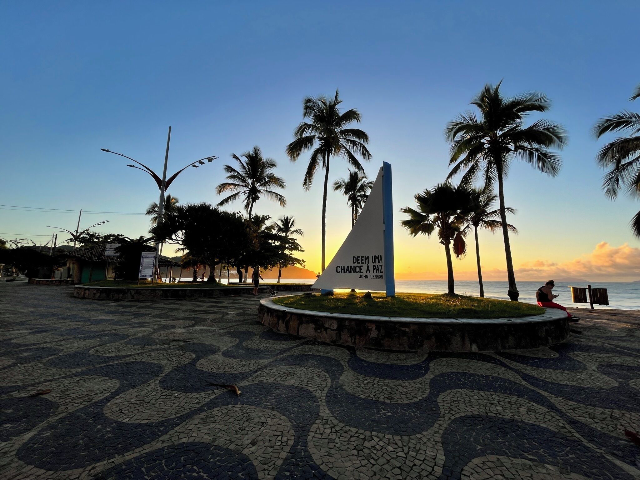 A paved area with a triangular monument and palm trees, overlooking a body of water.