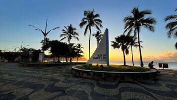 A paved area with a triangular monument and palm trees, overlooking a body of water.