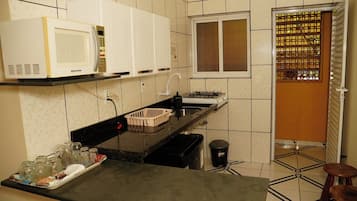 Una cocina compacta con microondas, estufa, fregadero y una ventana con celosía decorativa.