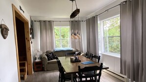 Ruokailutilassa on puinen pöytä ja tuolit, kattotuuletin ja näkymä vehreään maisemaan.