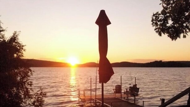 Laiturilta avautuva näkymä auringonlaskuun, laiturilla on tuoleja ja pöytä, ja näkymä on tyynelle vesialueelle.