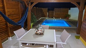 Un espace extérieur abrité comprenant une piscine, des murs en bois et une table avec des chaises.
