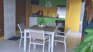 Un coin repas avec une table et des chaises, une cuisine avec des meubles verts et un four à micro-ondes placé au-dessus de l’évier.