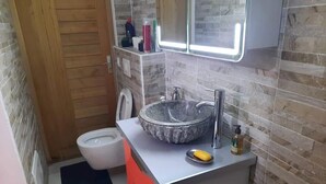 Une petite salle de bain dotée d’un lavabo en marbre, de toilettes et d’un miroir avec éclairage intégré.