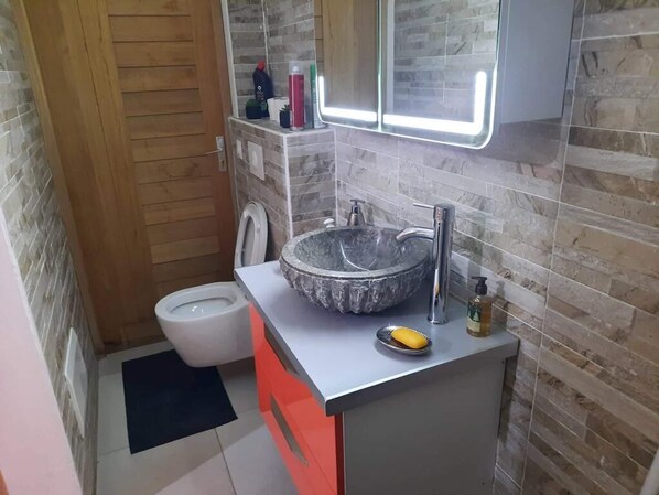 Une petite salle de bain dotée d’un lavabo en marbre, de toilettes et d’un miroir avec éclairage intégré.