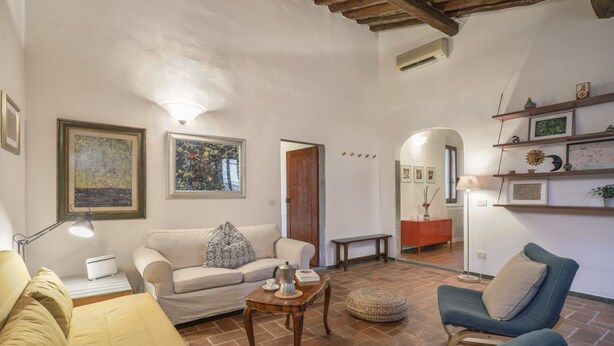 A living room with a sofa, armchair, and coffee table, a wooden bench, and a door leading to another room.