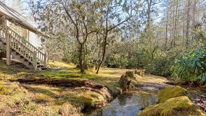 Una escalera de madera que conduce a una casa rodeada por un paisaje natural con un riachuelo y rocas cubiertas de musgo.